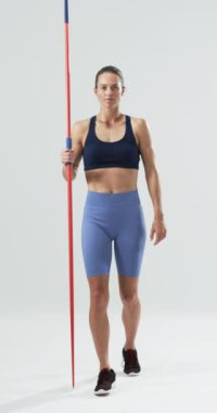 Dikey video: Güçlü ve formda bayan atlet mızrak tutuyor, spor kıyafetleri içinde güvenle poz veriyor. fitness, power, confidence, slow motion