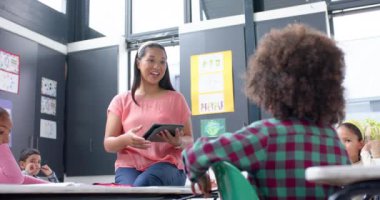 Okulda, öğretmen tablet tutuyor ve öğrencilere sınıf aktivitelerini öğretiyordu. Eğitim, öğrenme, öğretim, çocuklar, teknoloji, etkileşim, değiştirilmemiş, yavaş çekim