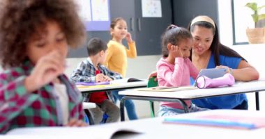 Okulda, öğretmenler öğrencilere sınıfta tabletle yardım ediyor, diğer öğrenciler okuyor. Eğitim, öğrenme, teknoloji, akademik, dijital, yardım, değiştirilmemiş, yavaş çekim