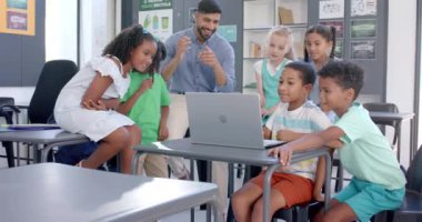 Öğretmenler okulda çeşitli öğrencilerle temas halindedir. Dizüstü bilgisayarın etrafındaki bir grup aktivitesine odaklanmışlar. Takım çalışmasını ve öğrenmeyi teşvik ediyorlar. Yavaş çekimde..