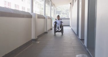 Okul koridorunda gezinen, tekerlekli sandalyedeki Afrikalı Amerikalı kız bağımsız hareket ediyor, önüne odaklanıyor. Eğitim, erişilebilirlik, bağımsızlık, hareketlilik, yetkilendirme, dahil etme