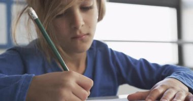 Okulda, sınıfta kurşun kalemle yazmaya konsantre olan bir çocuk. Eğitim, öğrenme, öğrenim, çocukluk, konsantrasyon