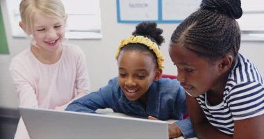 Okulda, üç kız birlikte dizüstü bilgisayar kullanıyor, proje üzerinde çalışıyorlar. Eğitim, takım çalışması, işbirliği, öğrenciler, teknoloji, sınıf