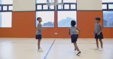 Okulun spor salonunda basketbol oynamak, top sürme ve pas yapma pratiği yapan üç çocuk. Spor, takım çalışması, egzersiz, antrenman, spor