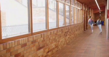 Okul koridorunda yürürken, el ele tutuşan ve gülümseyen iki kız, kopyalama alanı. Arkadaşlık, öğrenciler, mutluluk, çocukluk, birliktelik, eğitim