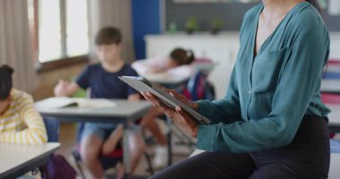 Okulda, öğrenciler sınıfta okurken öğretmen tablet kullanıyordu. Eğitim, teknoloji, öğretim, öğrenme, eğitmen, dijital