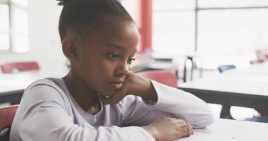Okulda, Afrikalı Amerikalı bir kız masada oturuyor, düşünceli görünüyor ve işine konsantre oluyor. Eğitim, öğrenim, eğitim, çocukluk, konsantrasyon, odaklanma