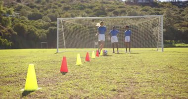 Futbol oynuyor, kız okul sahasında sınıf arkadaşları izlerken külahlarda top sürüyor. Spor, eğitim, egzersiz, takım çalışması, fiziksel aktivite, çocukluk