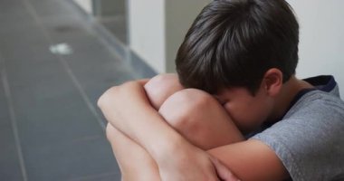 Ağlayan çocuk okul koridorunda yerde oturuyor, üzgün ve üzgün. Üzüntü, zorbalık, depresyon, yalnızlık, eğitim, çocukluk