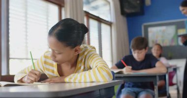 Okulda, masa başında not defterine yazı yazan bir kız, sınıf çalışmalarına odaklanıyor. Eğitim, öğrenim, öğrenim, çocukluk, akademik, ev ödevi