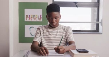Okulda, akıllı telefon ve kitaplarla not defterine yazı yazan Afro-Amerikalı genç bir çocuk vardı. Eğitim, sınıf, öğrenim, öğrenim, çocukluk, teknoloji