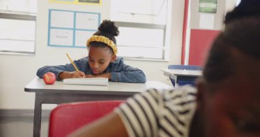 Okulda, masa başında elmalı not defterine yazan bir kız, işe odaklanıyor. Eğitim, öğrenim, öğrenme, çocukluk, ödev, konsantrasyon