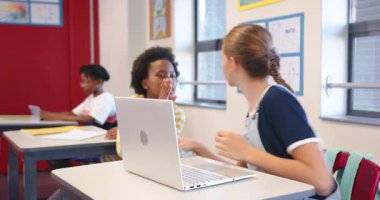 Okulda, sınıf arkadaşları konuşurken dizüstü bilgisayar kullanan bir kız. Eğitim, teknoloji, öğrenme, öğrenim, dijital