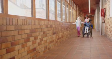 Okulda, iki kız tekerlekli sandalyeyle arkadaşını koridorda itiyor, gülümsüyor ve sohbet ediyor. Eğitim, arkadaşlık, kapsama, çeşitlilik, destek, neşe