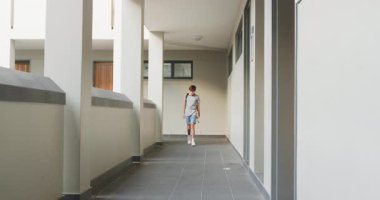 Okul koridorunda yürürken, sırt çantası taşıyan ve klasörü tutan bir çocuk. Eğitim, öğrenci, öğrenim, gençlik, akademik, öğrenim