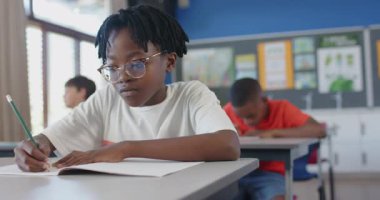 Okulda, masa başında not defterine yazan bir çocuk, işine konsantre oluyor. Eğitim, okula dönüş, öğrenme, öğrenme, sınıf, çocukluk