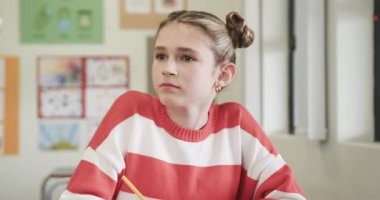 Okulda, sınıfta, çizgili süveter giymiş, dikkatle yazan genç bir kız. Eğitim, öğrenim, öğrenim, genç kız, odaklanma, konsantrasyon