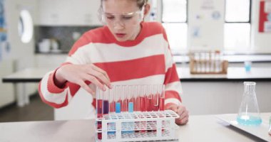 Fen sınıfında elinde test tüpleri olan genç bir kız okulda heyecan verici bir şekilde deney yapıyor. lab, kimya, deney, eğitim, araştırma, laboratuvar