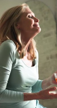 Dikey video: Gülümseyen son sınıf öğrencisi kadın neşeli ve rahat bir şekilde evinde eğleniyor. Yaşlı, tatil, kutlama, mutluluk, neşeli, rahat