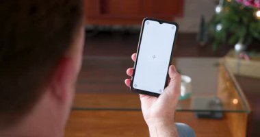 Noel zamanı evde elinde boş ekranlı akıllı telefon tutan bir adam. Teknoloji, tatil, kutlama, dekorasyon, dijital, mobil