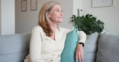 Gülümseyen son sınıf öğrencisi kadın evde kahveyle kanepede dinleniyor, kendini mutlu hissediyor. Rahatlama, mutluluk, rahatlama, yaşlı yetişkin, rahat, huzurlu