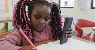 Sınıfta, okulda akıllı telefonu dikkatle tutarken deftere yazı yazan genç bir kız. kız, çoklu görev, konsantrasyon, teknoloji, eğitim, öğrenim