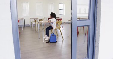 Genç kız sırt çantasıyla sınıfa giriyor, okul gününe hazırlanıyor. Eğitim, okula dönüş, öğrenme, kız, çocukluk