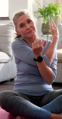Dikey video: Yaşlı kadın evde yoga minderinde geriniyor, sağlıklı yaşam tarzını kucaklıyor. Sağlık, fitness, egzersiz, meditasyon, denge, esneklik
