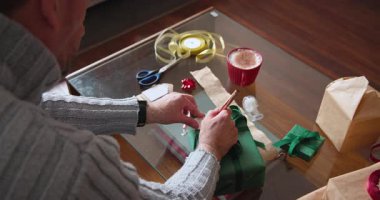 Son sınıf öğrencisi Noel hediyesini tahta masaya kurdele ve künyeyle paketliyor. Tatil, şenlikli, mevcut, mevsimlik, yaşlı, el işi.