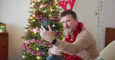 Akıllı telefondan son sınıf videosu aranıyor, Noel ağacının yanında boynuz takıyor. Tatiller, kutlamalar, teknoloji, dekorasyon, kış mevsimi, neşeli