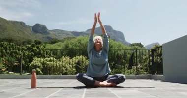 Üst düzey kadın yoga minderinde balkonda meditasyon yapıyor, huzur dolu dağ manzarasının tadını çıkarıyor. Meditasyon, sağlık, sükunet, rahatlama, farkındalık, manzara