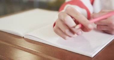 Okul masasında pembe kalemle not defterine yazan genç bir kız, dikkatle odaklanıyor. Eğitim, öğrenim, öğrenim, konsantrasyon, sınıf, akademik