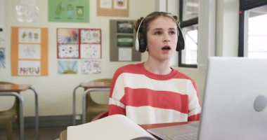 Video konuşmasında, okulda kulaklık takan bir kız online sınıf tartışmasına giriyor. E-öğrenme, uzaktan öğrenme, teknoloji, eğitim, öğrenim, sanal sınıf