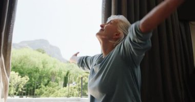 Yaşlı kadın evde yoga yapıyor, pencerenin önünde huzurlu dakikaların tadını çıkarıyor. Sağlık, farkındalık, dinginlik, fitness, egzersiz, meditasyon