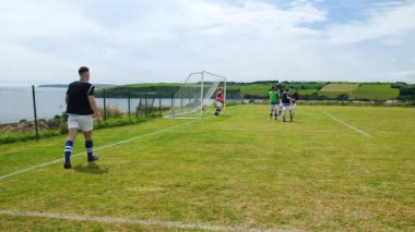 Futbolcular sahile yakın sahada antrenman yapıyor, maça hazırlanıyorlar. Sporcular, antrenman, takım çalışması, fitness, rekabet, hazırlık