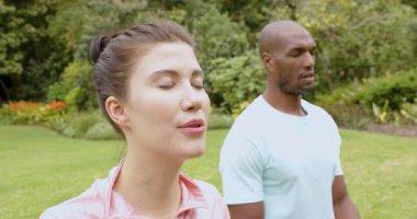 Dışarıda yoga yapan çok ırklı bir çift parkta rahatlamaya ve farkındalığa odaklanıyor. Meditasyon, sağlık, egzersiz, sükunet, zindelik