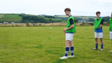 Futbolcu, göl ve tepelerin yakınındaki çimenlik alanda topa vuruyor. Spor, atlet, doğa, açık hava, rekabet, manzara