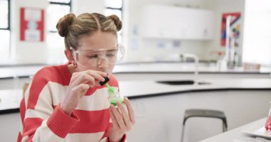 Okulda, güvenlik gözlüğü takan bir kız odaklanarak bilim deneyi yapıyor. STEM, lab, eğitim, öğrenme, kimya, sınıf