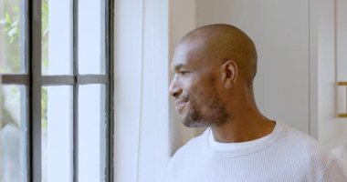 Gülümseyen Afro-Amerikan adam pencereden dışarı bakıyor, evinde huzurlu bir anın tadını çıkarıyor. Düşünce, sükunet, rahatlama, mutluluk, huzur, yaşam tarzı
