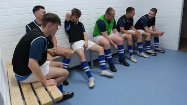 Futbol takımı soyunma odasında hazırlanıyor, ayakkabı bağlıyor ve strateji tartışıyorlar. Spor, takım çalışması, hazırlık, sporcular, yoldaşlık, yarışma