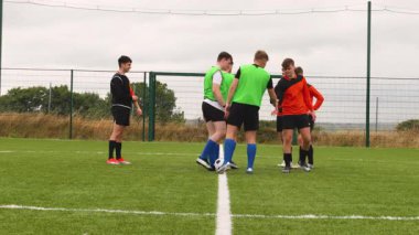 Futbolcular yeşil yeleklerle açık havada başlama vuruşuna hazırlanıyorlar. Spor, sporcular, takım çalışması, rekabet, strateji, eğitim