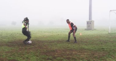 Futbolcular sisli sahada antrenman yapıyor, kaleci topu kurtarmak için dalıyor. Futbol, kaleci, antrenman, atletizm, takım çalışması, savunma