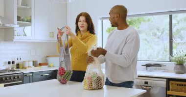 Modern mutfaktaki alışveriş paketlerini açan, evde gülümseyen çok ırklı bir çift. aile, yaşam tarzı, yerli, ilişki, alışveriş