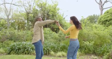 Çeşitli çok ırklı çiftler parkta neşeyle dans ediyor, güneşli günlerin tadını çıkarıyorlar. Aşk, dans, açık hava, mutluluk, yaşam tarzı, güneş ışığı.