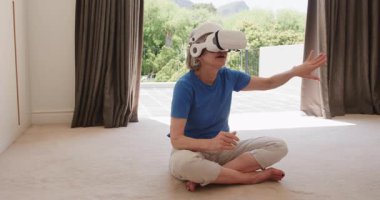 VR kulaklık takan yaşlı bir kadın evde, yerde otururken sanal dünyayı keşfediyor. Teknoloji, sanal gerçeklik, yaşlılık, yenilik, dalgın, keşif