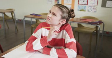 Okulda, masa başında not defterine yazı yazan bir kız, ödevine konsantre oluyor. Eğitim, öğrenim, öğrenim, genç kız, sınıf, odaklanma