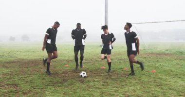 Siyah üniformalı futbolcular sisli alanda gülüyor ve dinleniyorlar. Takım çalışması, yoldaşlık, sporcular, eğlence, kaynaşma, sportmenlik.