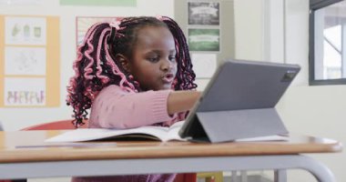 Sınıfta, Afro-Amerikan kız tablet ve kitapla çalışıyor, okula odaklanmış görünüyor. Eğitim, teknoloji, okul, öğrenme, akademik, konsantrasyon
