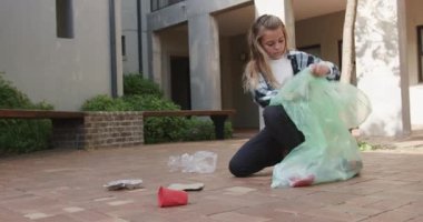 Genç kız dışarıdaki çöpleri temizliyor, yeşil torba içinde çöp topluyor, okulda. Çevre, sürdürülebilirlik, geri dönüşüm, temizlik, gönüllü, doğa