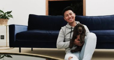 Evde oturmuş gülümseyen Asyalı adam, sevimli bir köpeği okşuyor. yoldaşlık, mutluluk, dostluk, evcil, rahatlama, yaşam tarzı